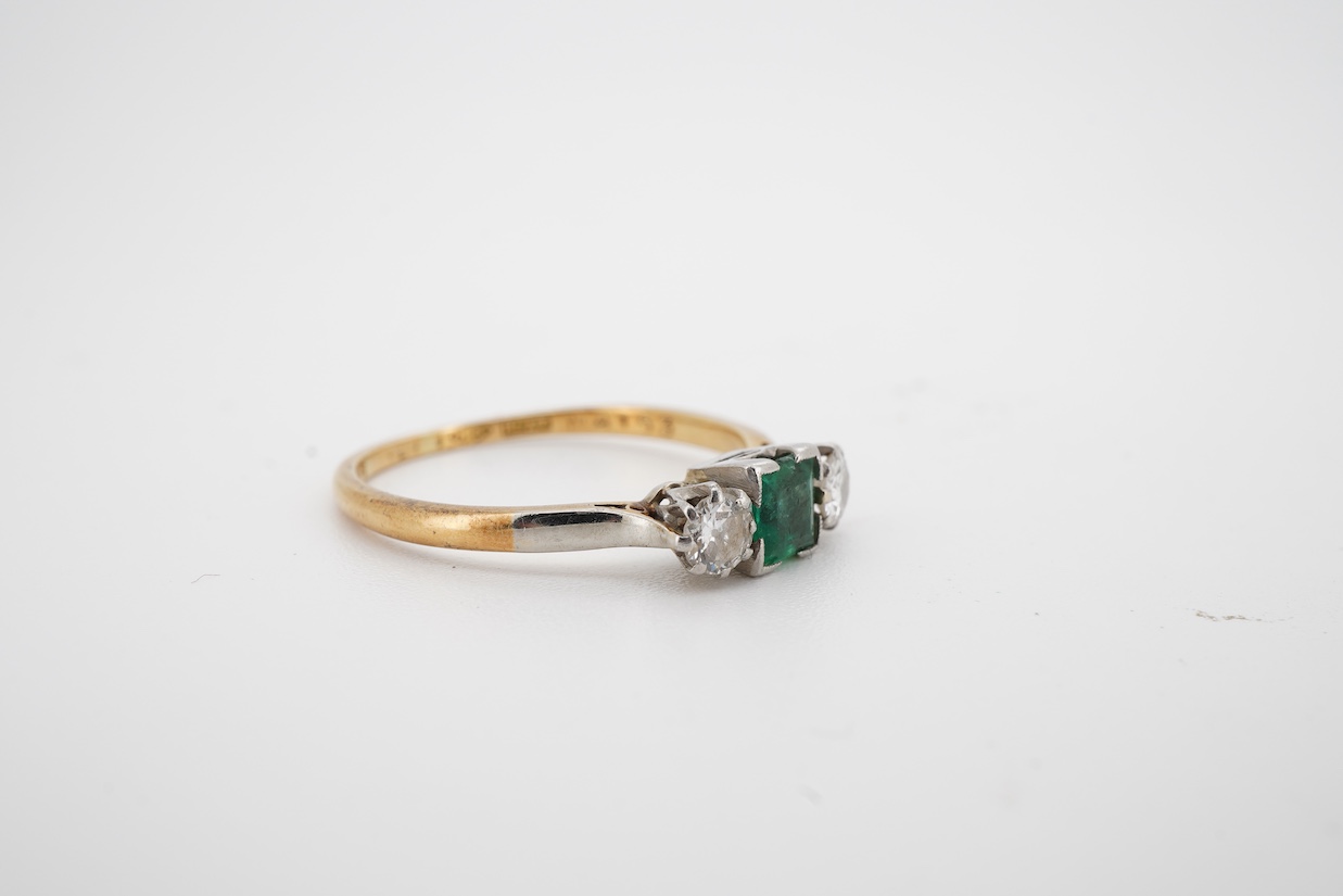 A yellow metal, single stone emerald and two stone diamond set ring, the emerald measuring approximately 4.3mm, the diamonds approximately 0.15ct each, the shank stamped with maker's mark HS and 'Plat', size P/Q.